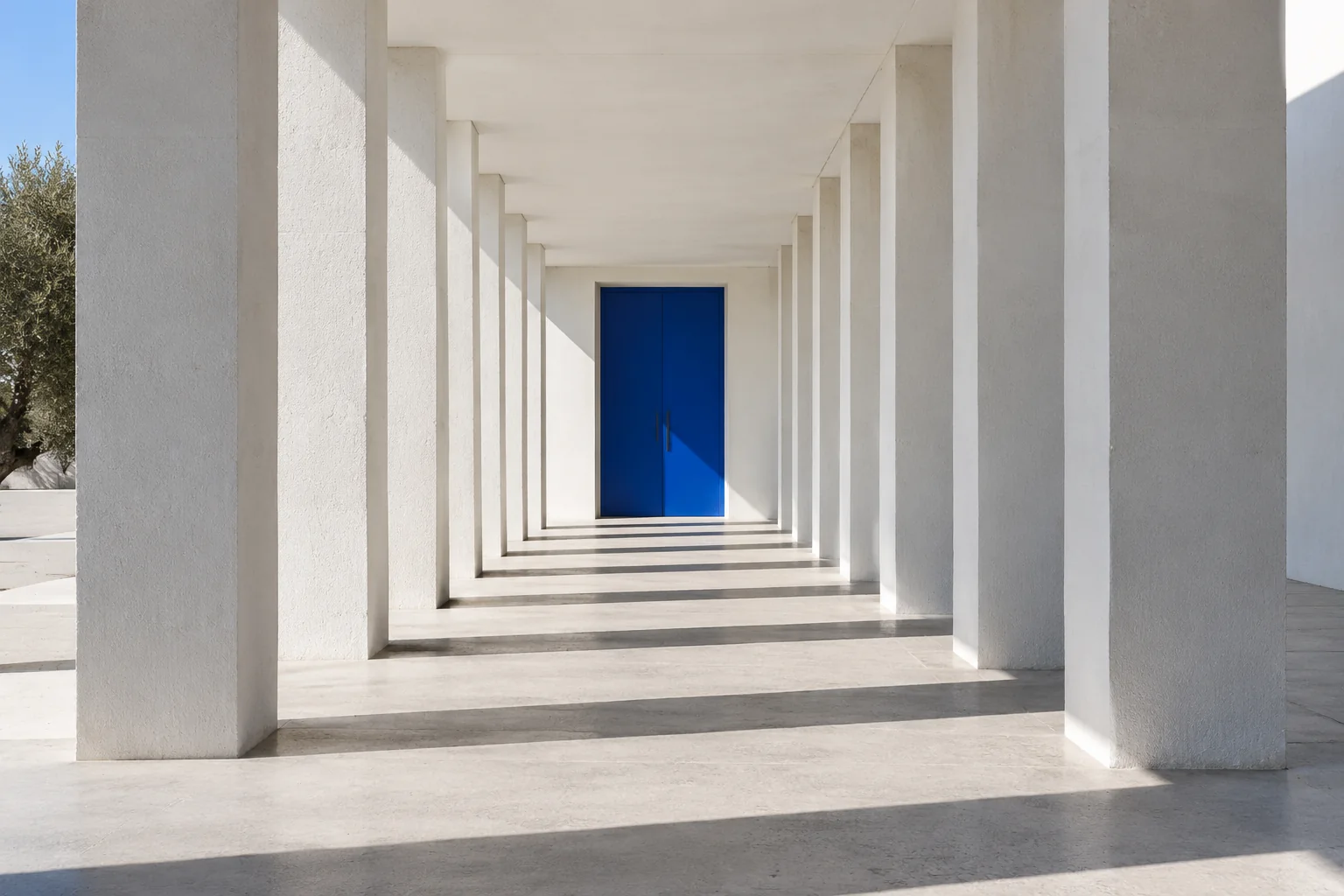 A single cobalt doorway at the end of a bright white architectural corridor