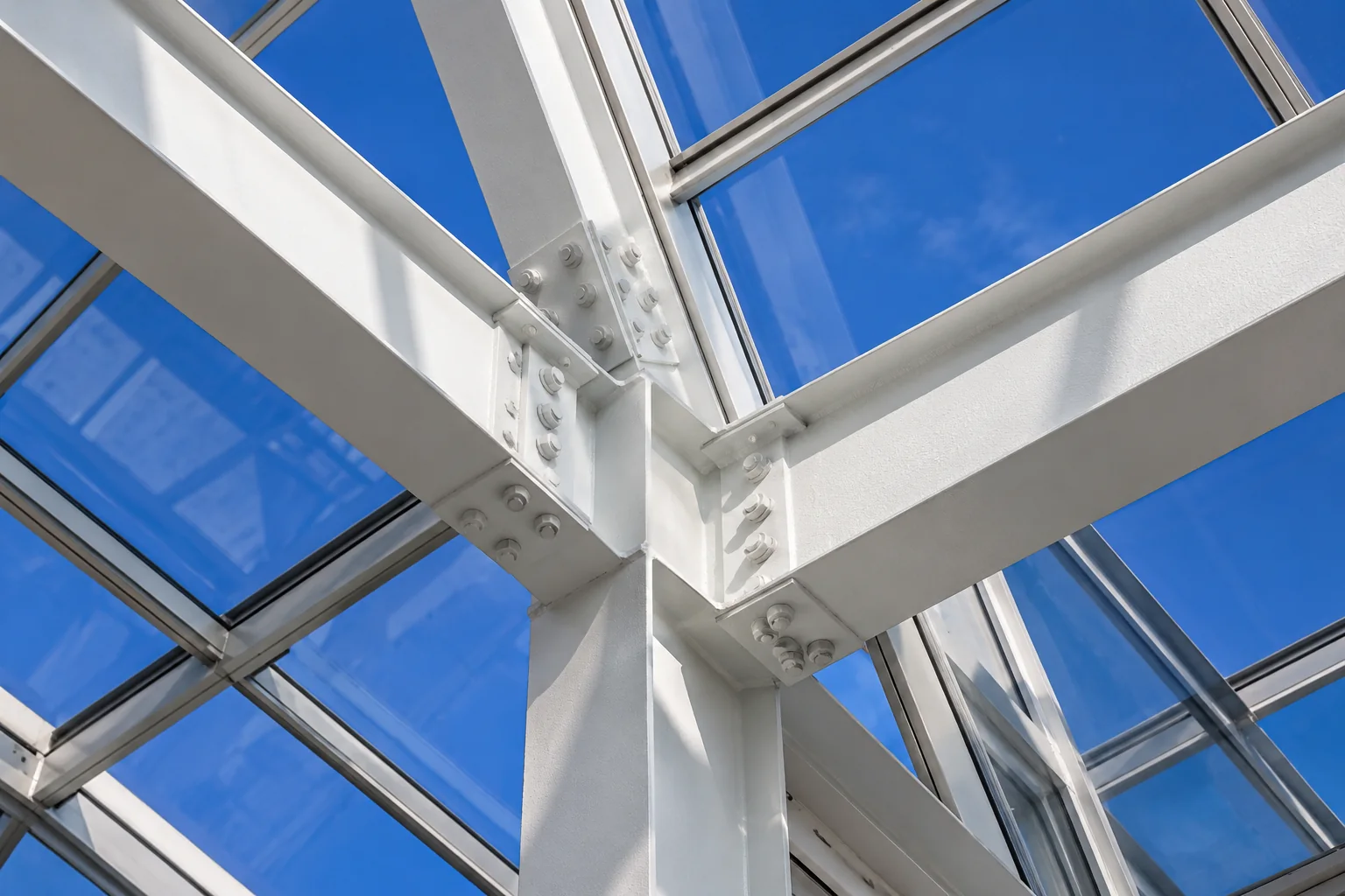 White structural beams and glass panels framing a vivid blue sky