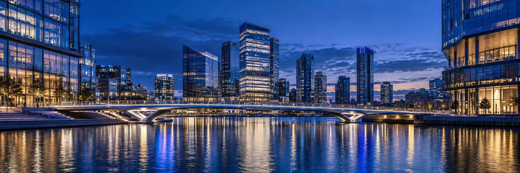 Contemporary waterfront architecture at blue hour, with illuminated glass buildings and a sweeping bridge